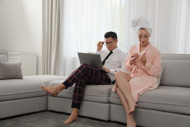 Photo of Man working on laptop while his wife relaxing in living room. Stay at home concept