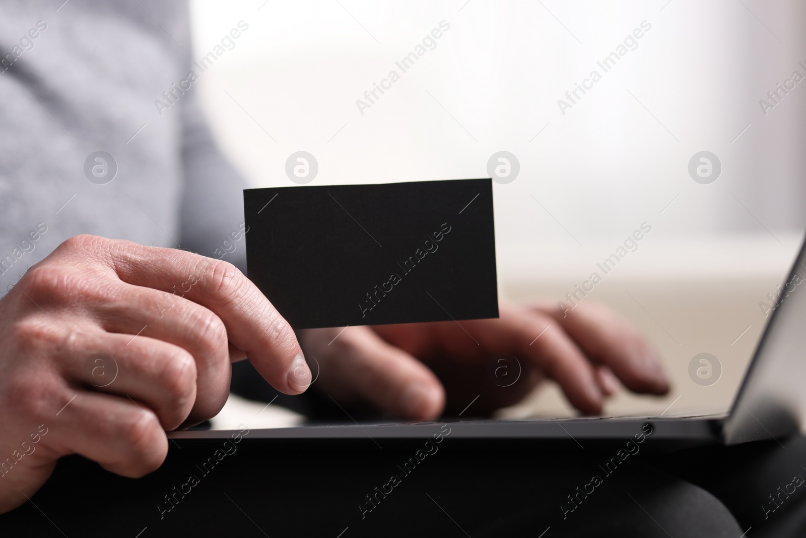 Photo of Man with laptop holding blank business card on blurred background, closeup