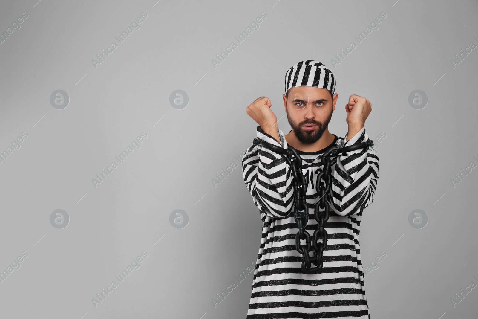 Photo of Prisoner in special uniform with chained hands on grey background, space for text
