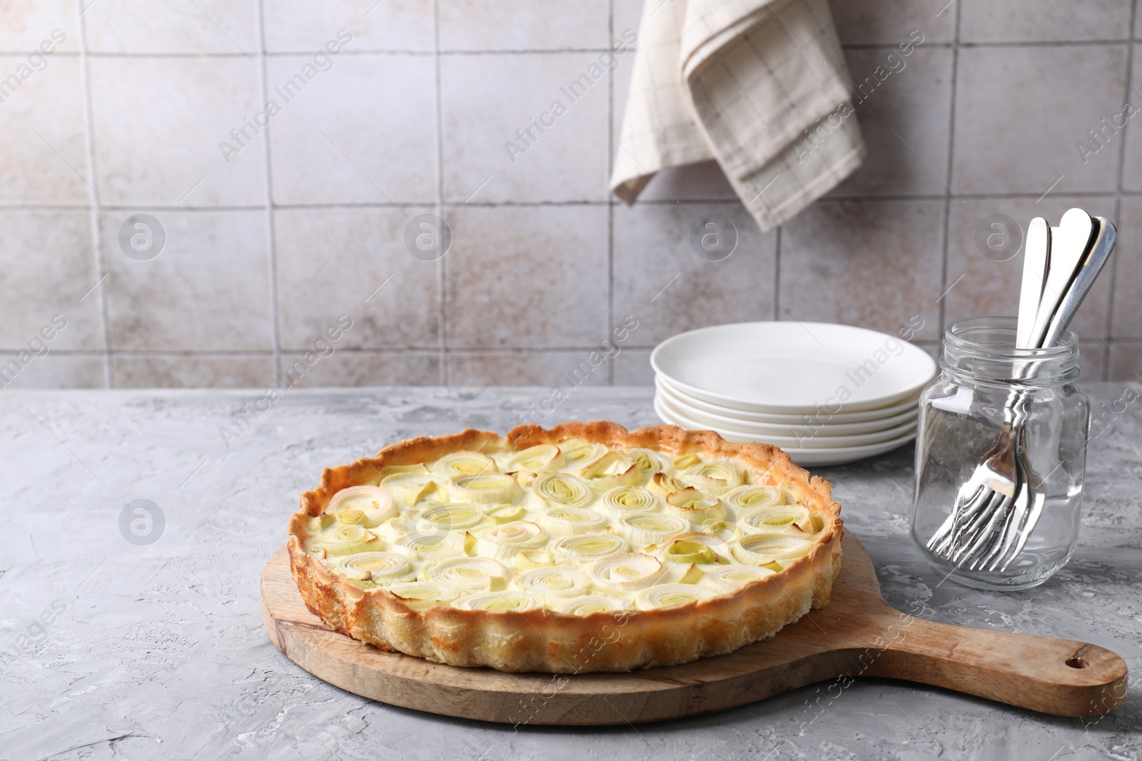 Photo of Freshly baked leek pie, forks and plates on grey textured table. Space for text