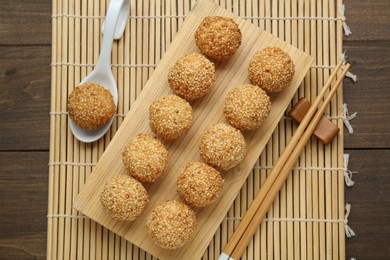 Delicious sesame balls, spoon and chopsticks on wooden table, flat lay