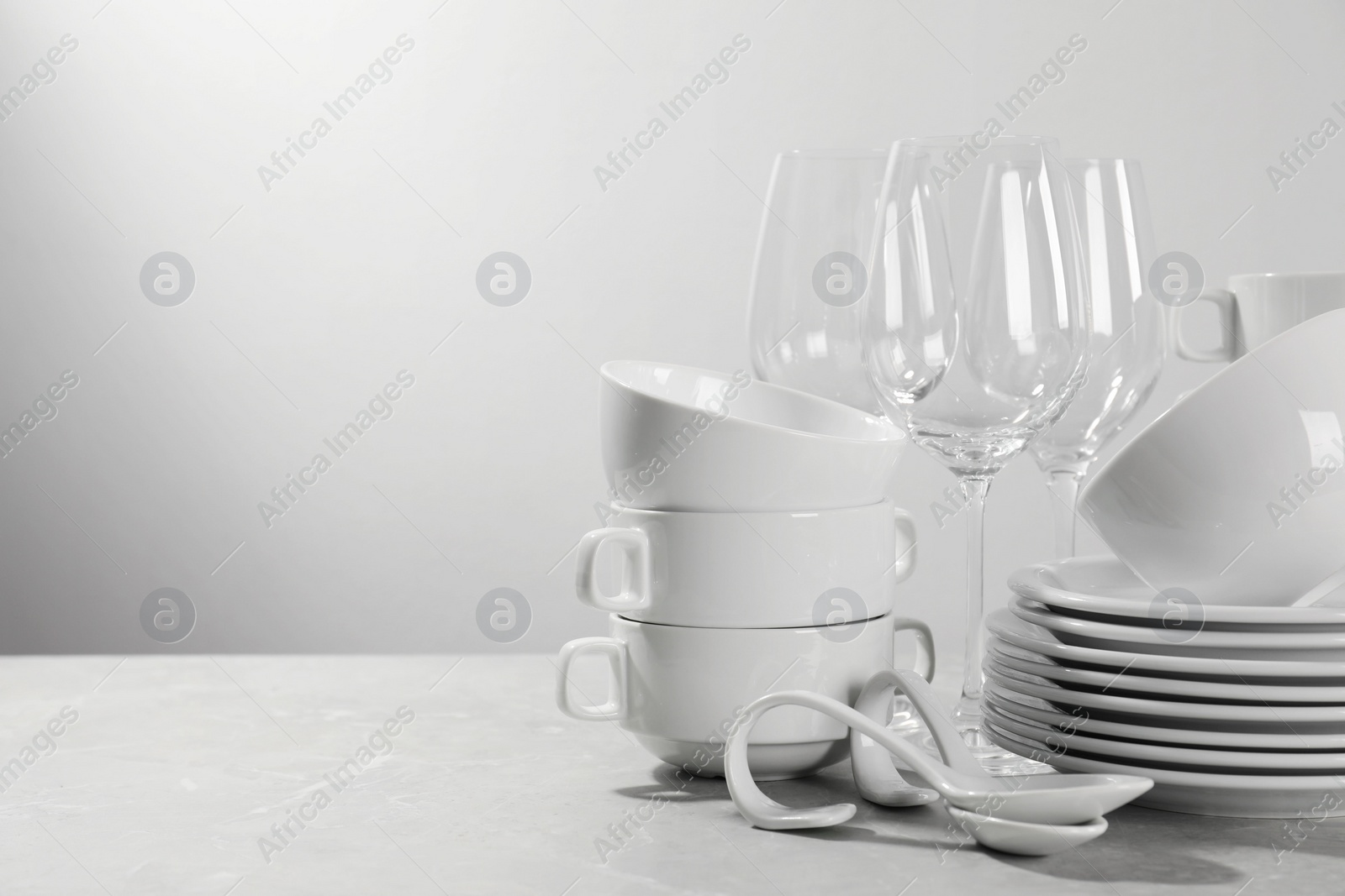 Photo of Set of clean dishware and glasses on grey table against light background. Space for text