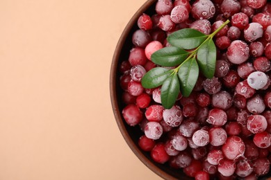 Photo of Frozen red cranberries and green leaves on beige background, top view. Space for text