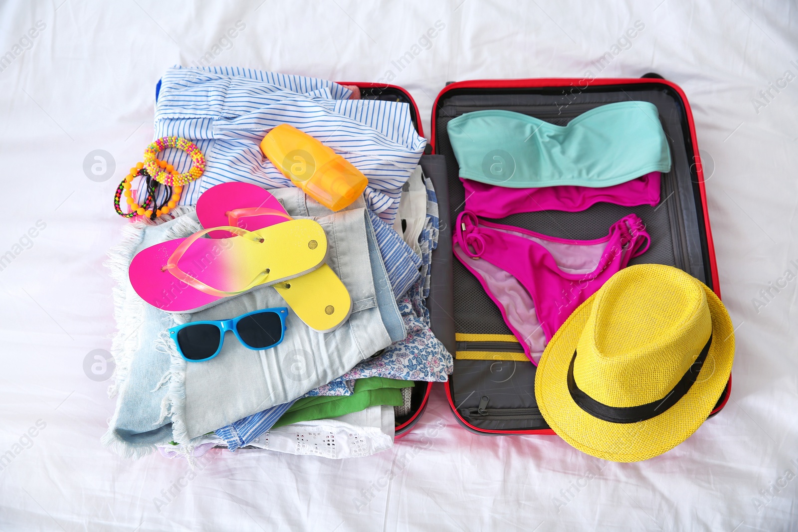 Photo of Open suitcase with different clothes and accessories for summer journey on bed