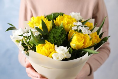 Woman with bouquet of beautiful tulips on light blue background, closeup