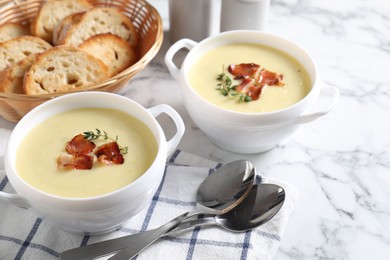 Photo of Tasty potato soup with bacon and rosemary in bowls served on white marble table