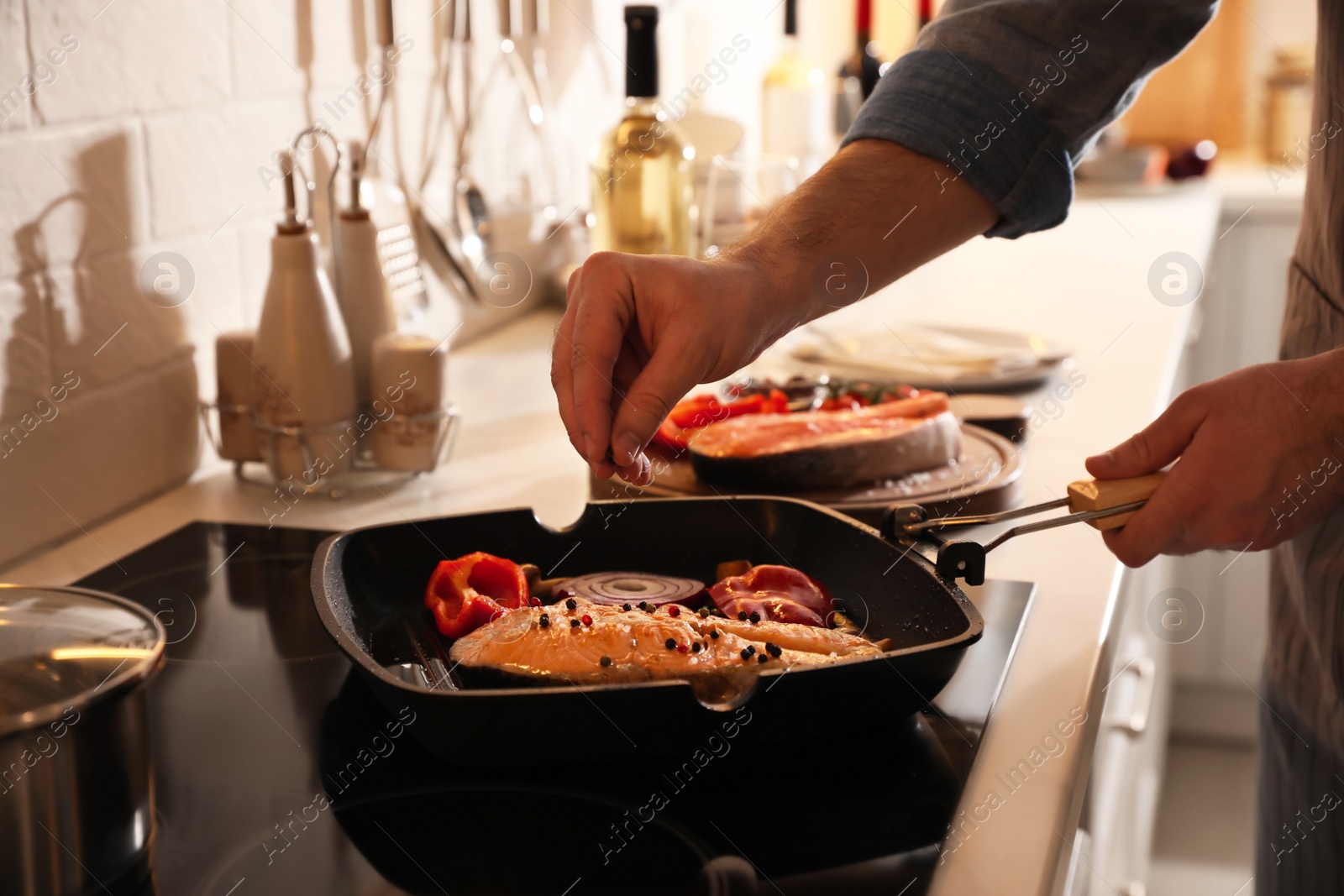 Photo of Man pouring pepper into frying pan with tasty salmon steak and vegetables, closeup