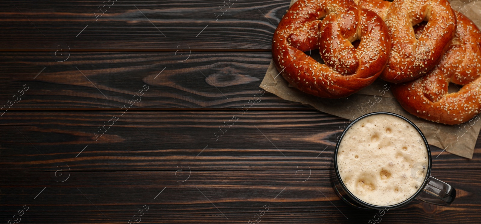 Image of Tasty freshly baked pretzels and mug of beer on wooden table, flat lay with space for text. Banner design