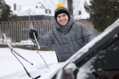 Photo of Happy man cleaning snow from car outdoors