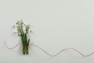 Photo of Beautiful snowdrops with traditional cord martisor on white background, flat lay and space for text. Symbol of first spring day