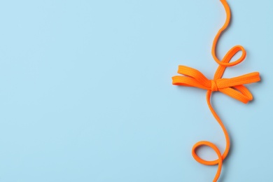 Photo of Orange shoelace on light blue background, top view. Space for text