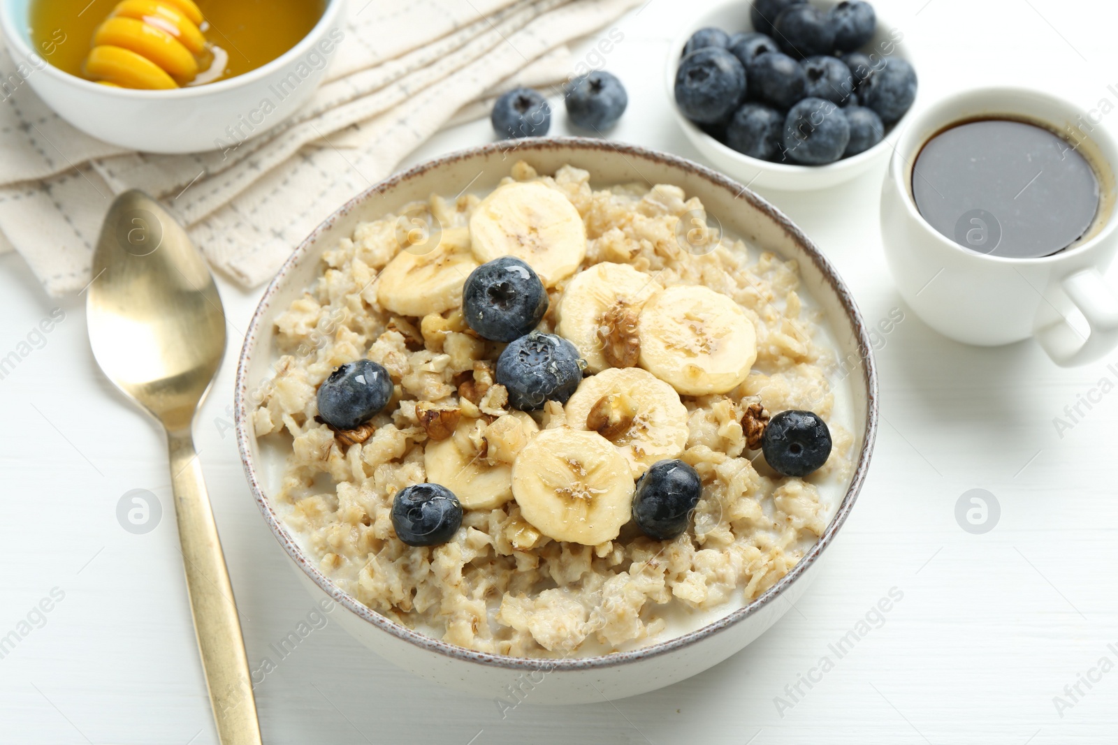 Photo of Tasty oatmeal with banana, blueberries, walnuts and honey served in bowl on white wooden table