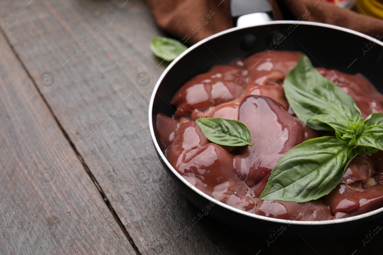 Photo of Raw chicken liver with basil in frying pan on wooden table, closeup. Space for text
