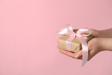 Woman holding gift box with bow on pink background, closeup. Space for text