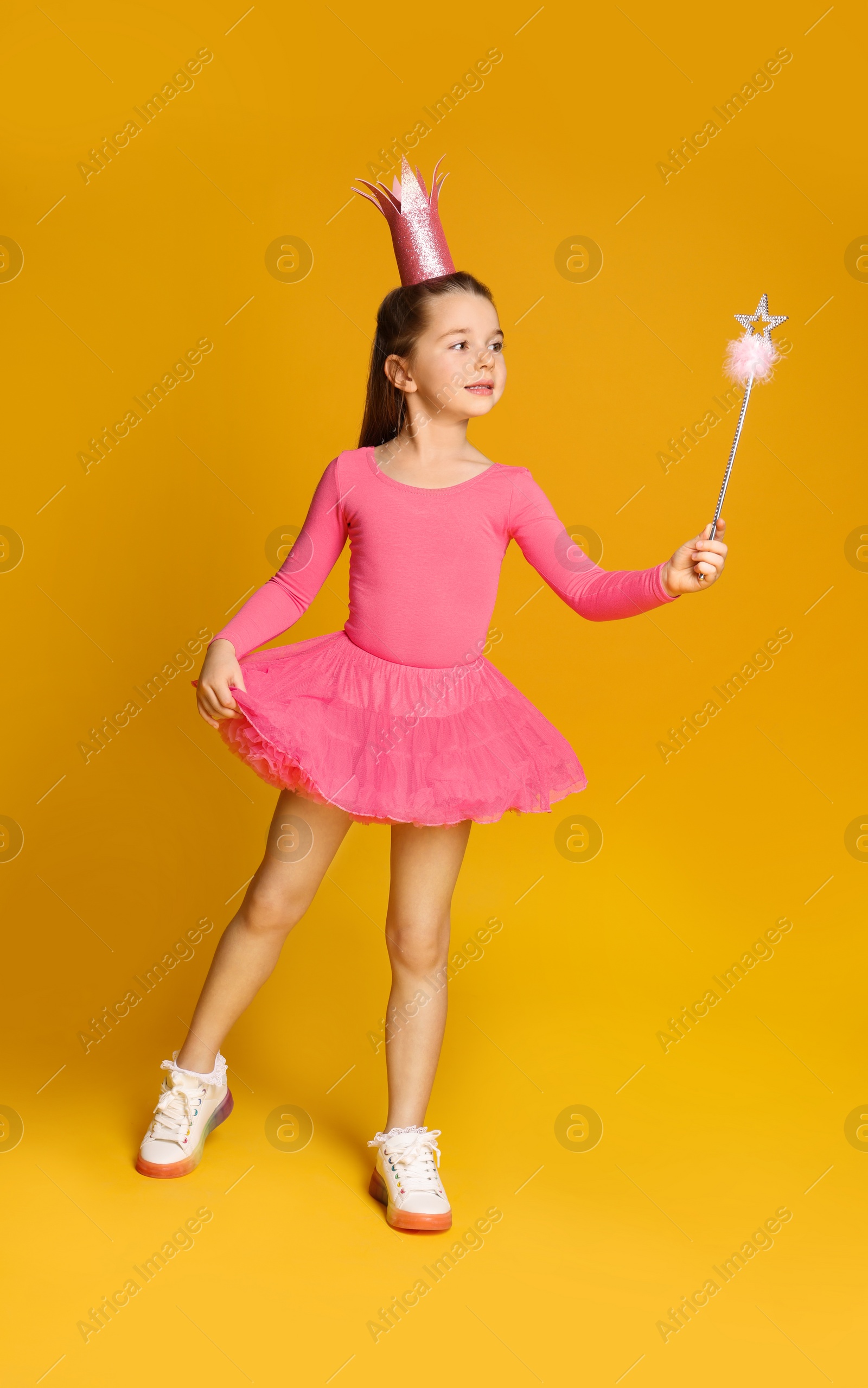 Photo of Cute girl in pink crown with magic wand on yellow background. Little princess