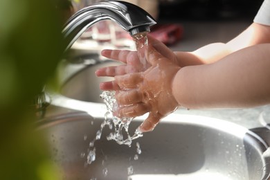 Photo of Little child washing hands in kitchen, closeup view