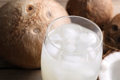 Photo of Glass of coconut water, ice cubes and nuts on wooden table, closeup