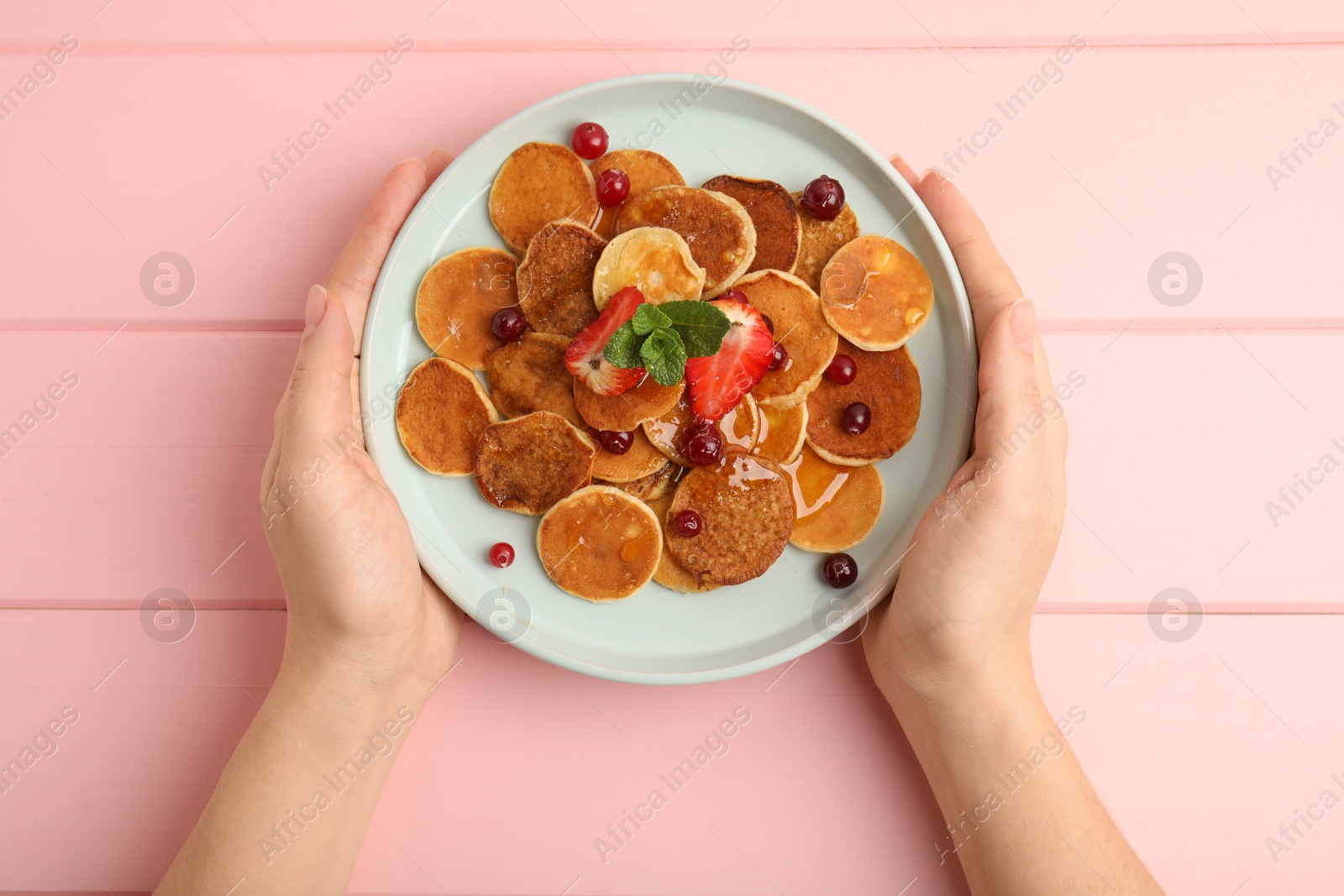 Photo of Woman holding plate with cereal pancakes at pink wooden table, top view