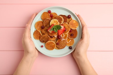 Woman holding plate with cereal pancakes at pink wooden table, top view