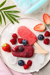 Plate of tasty berry ice pops on light wooden table, flat lay. Fruit popsicle