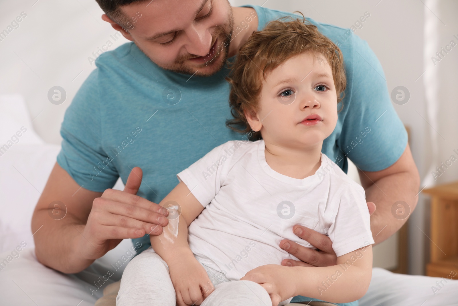 Photo of Father applying ointment onto his son`s arm on bed at home