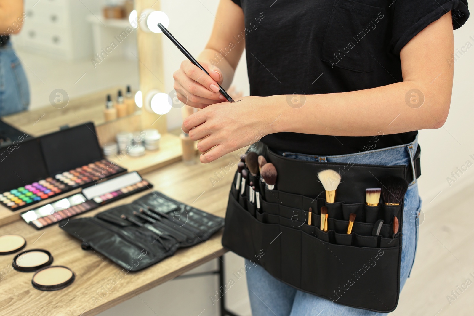 Photo of Professional makeup artist with belt organizer full of tools working in studio, closeup