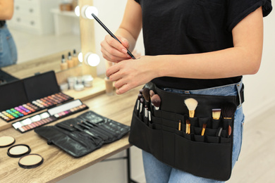 Photo of Professional makeup artist with belt organizer full of tools working in studio, closeup