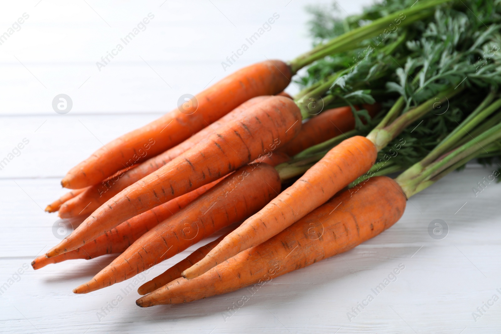 Photo of Ripe carrots on white wooden table, closeup