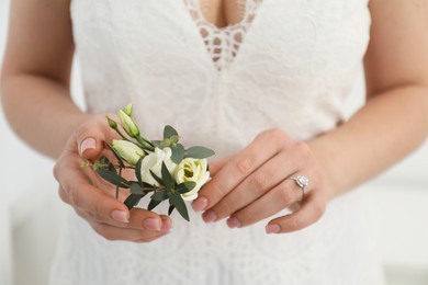 Bride holding boutonniere for her groom on blurred background, closeup