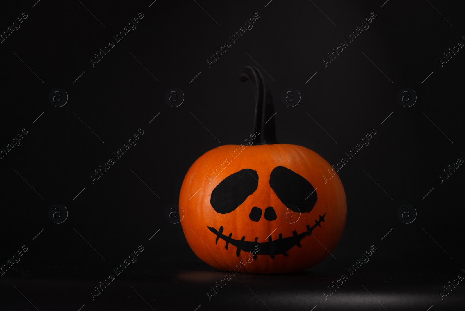 Photo of Halloween celebration. Pumpkin with drawn face on table in darkness, space for text