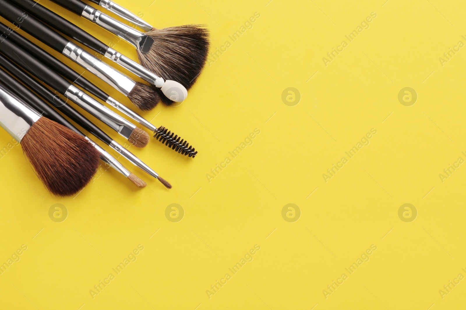 Photo of Set of makeup brushes on yellow background, flat lay. Space for text