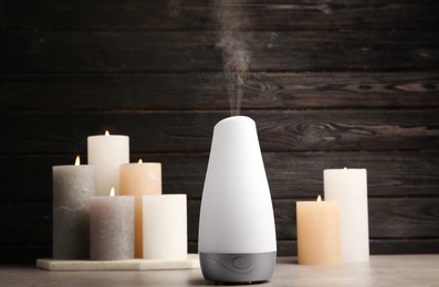 Modern aroma humidifier with candles on table against dark wooden background, space for text