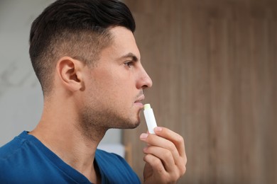 Handsome man applying hygienic lip balm indoors