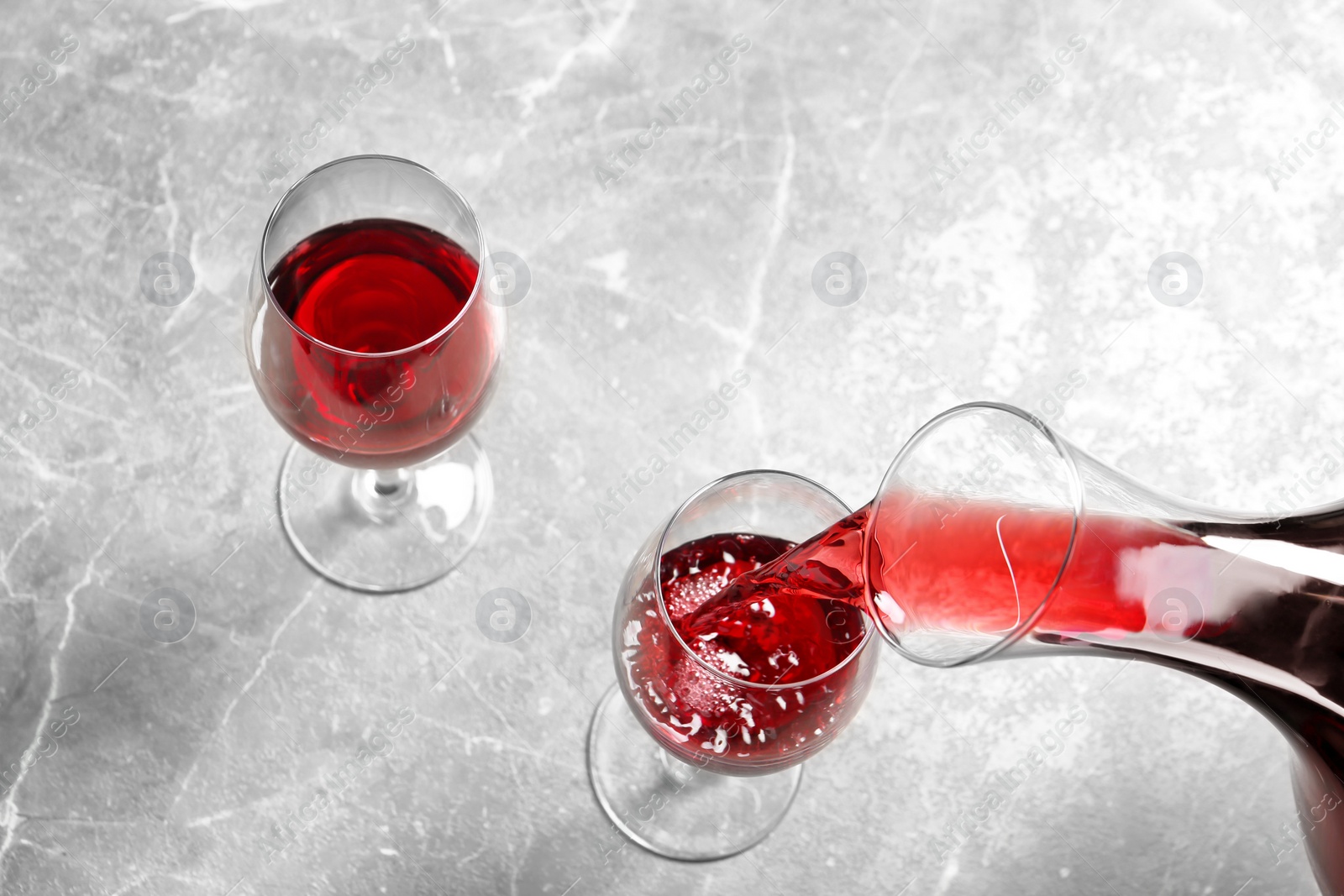 Photo of Pouring delicious red wine into glass on grey table, above view