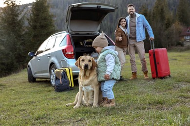 Photo of Dog, cute little girl and her parents near car in mountains. Family traveling with pet