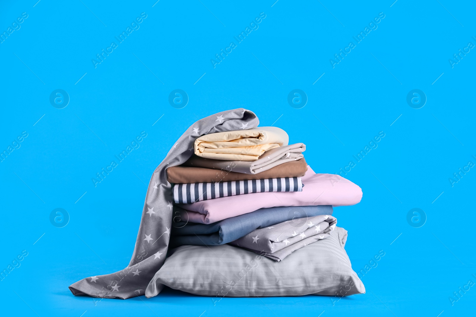 Photo of Stack of clean bed sheets and pillow on blue background