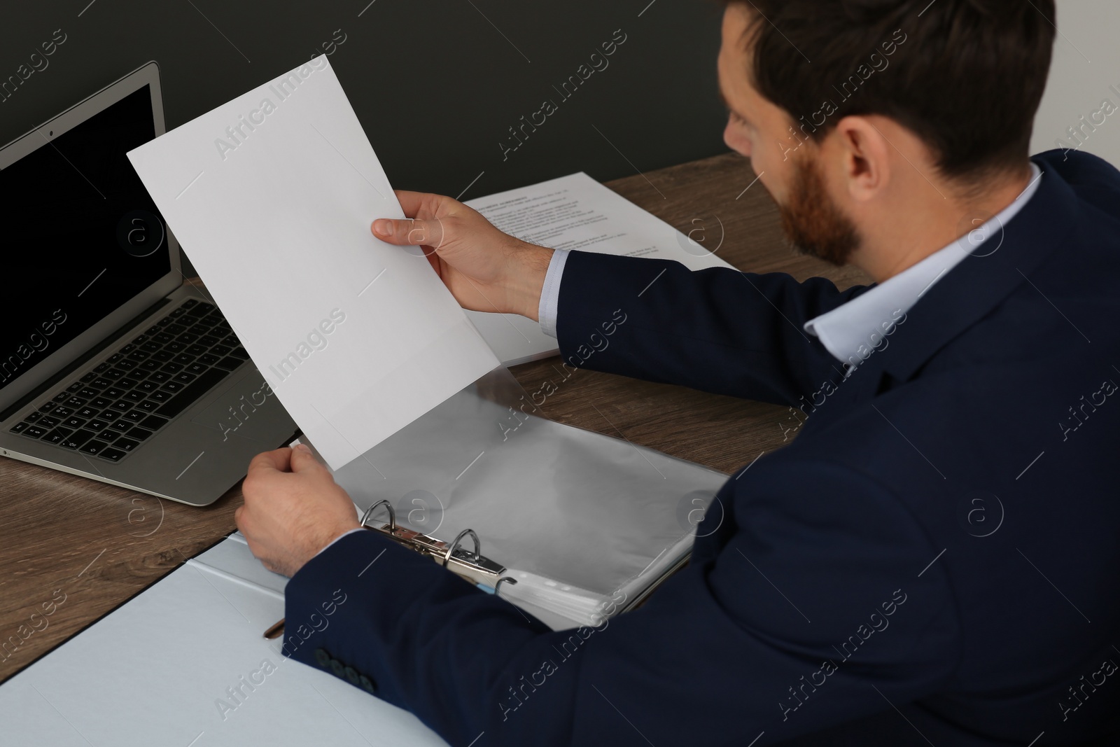 Photo of Businessman putting document into punched pocket at wooden table in office