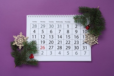 Composition with calendar, fir branches and Christmas decorations on purple background, flat lay. Boxing day concept
