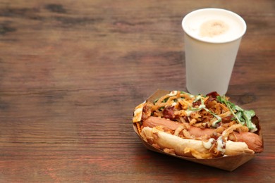 Photo of Fresh delicious hot dog and paper cup of coffee on wooden table, space for text