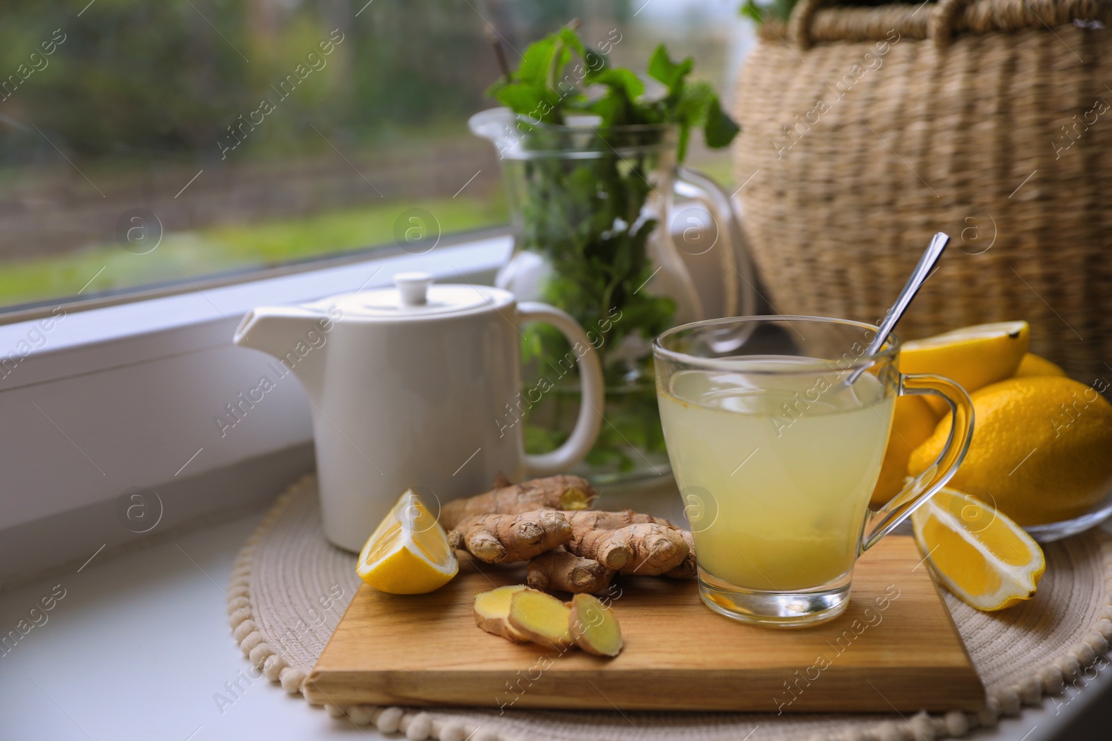 Photo of Glass of aromatic ginger tea and ingredients near window, space for text