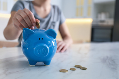 Photo of Woman putting money into piggy bank at marble table indoors, closeup. Space for text