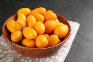 Photo of Fresh ripe kumquats in bowl on black table, closeup