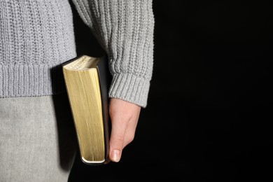 Photo of Woman holding Bible against black background, closeup. Space for text