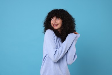 Happy young woman in stylish warm sweater on light blue background