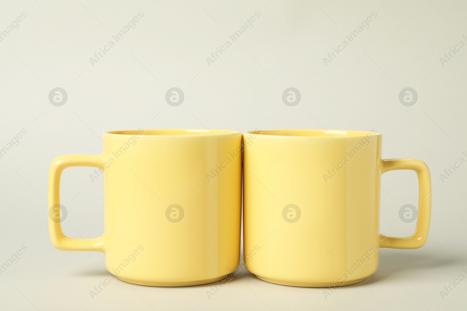 Photo of Two yellow ceramic mugs on light grey background