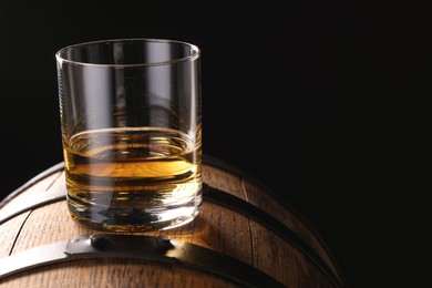 Whiskey in glass on wooden barrel against dark background, space for text