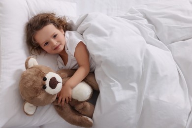 Photo of Cute little girl lying with teddy bear on bed, top view