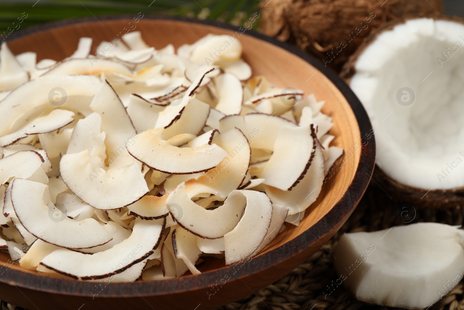 Photo of Tasty coconut chips in wooden bowl, closeup