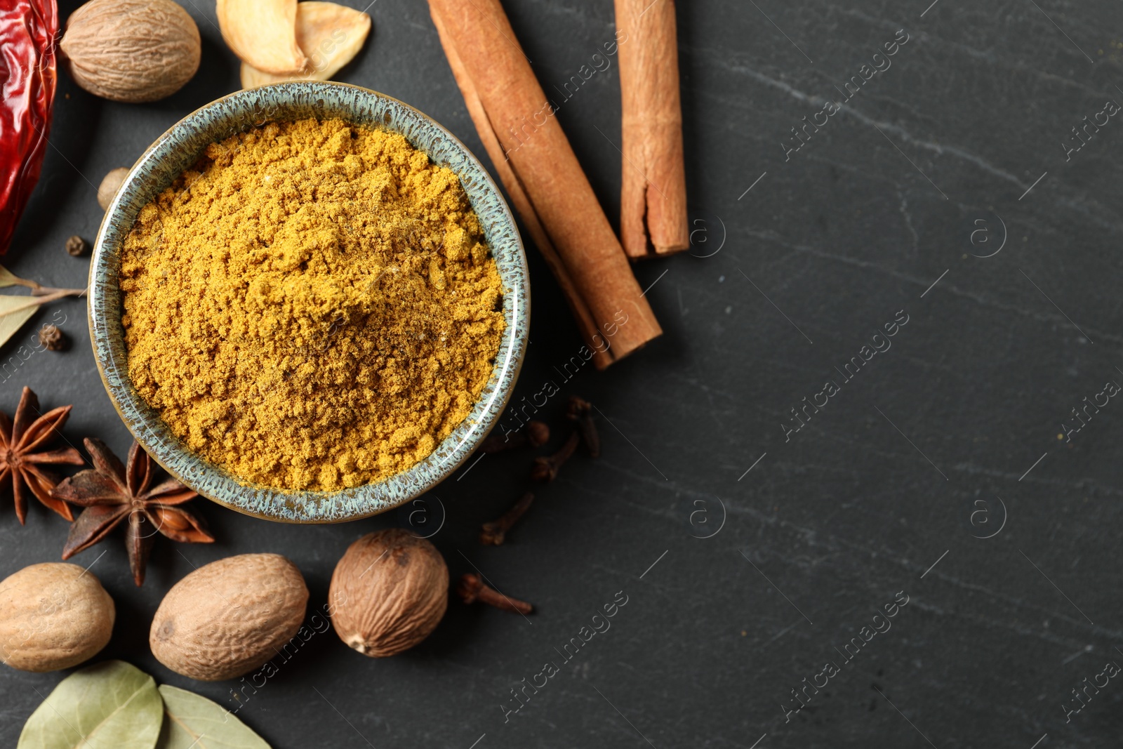 Photo of Dry curry powder in bowl and other spices on dark textured table, flat lay. Space for text