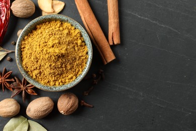 Photo of Dry curry powder in bowl and other spices on dark textured table, flat lay. Space for text